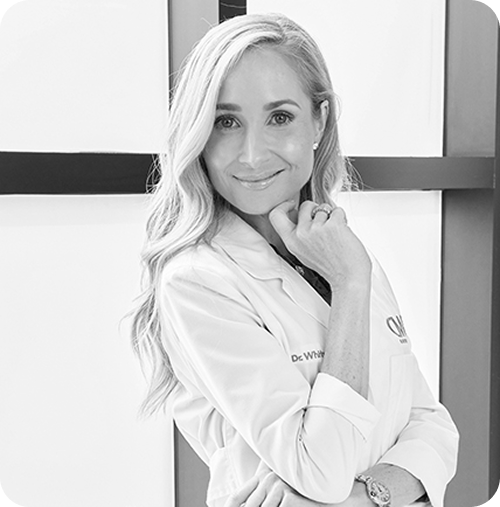 Woman in a white coat with 'Dr. White' on it, standing against a plain background