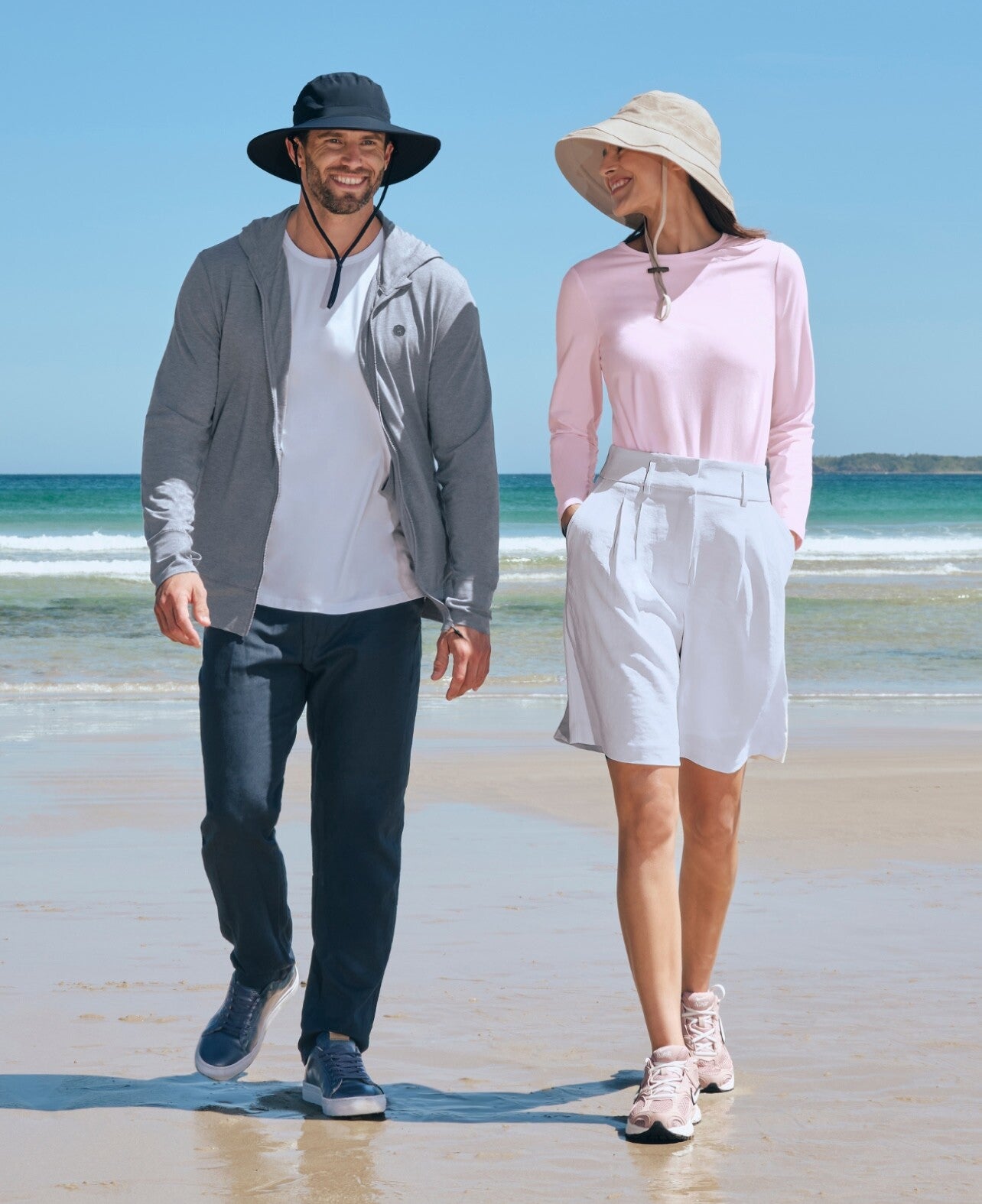Man and woman walking on a beach wearing Solbari sun hats and sun protective casual clothing.